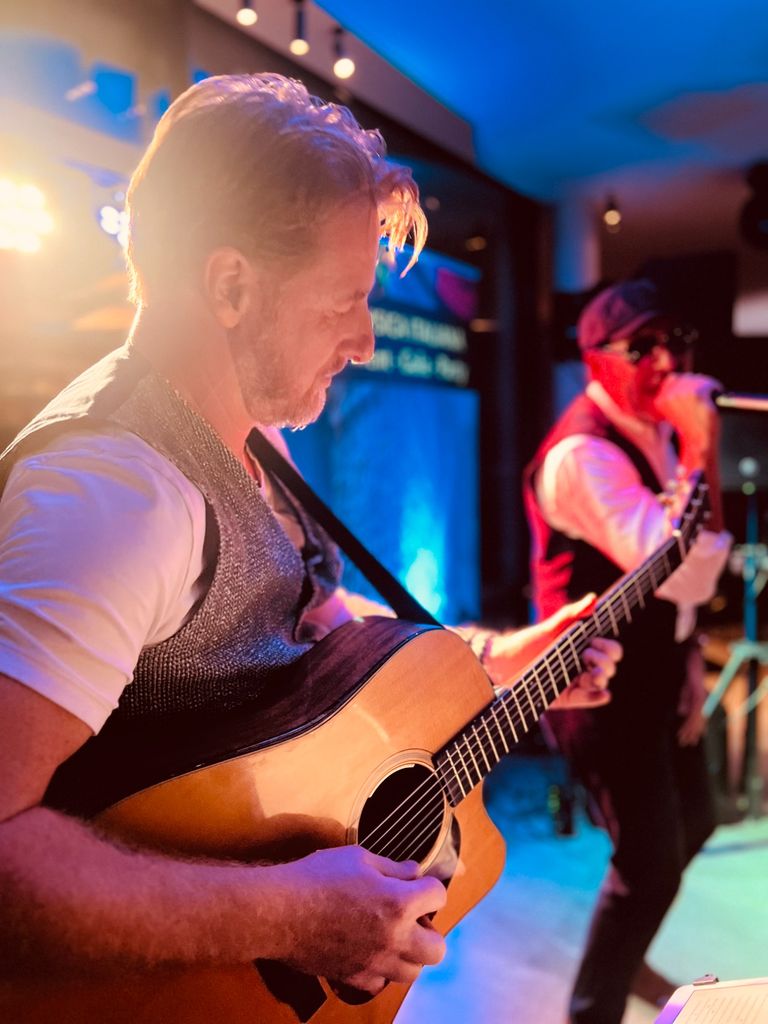 Mann spielt Akustikgitarre im Scheinwerferlicht, im Hintergrund singt ein Adriano Celentano Double